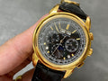 Gold wristwatch with black leather strap and black chronograph dial, visible subdials.