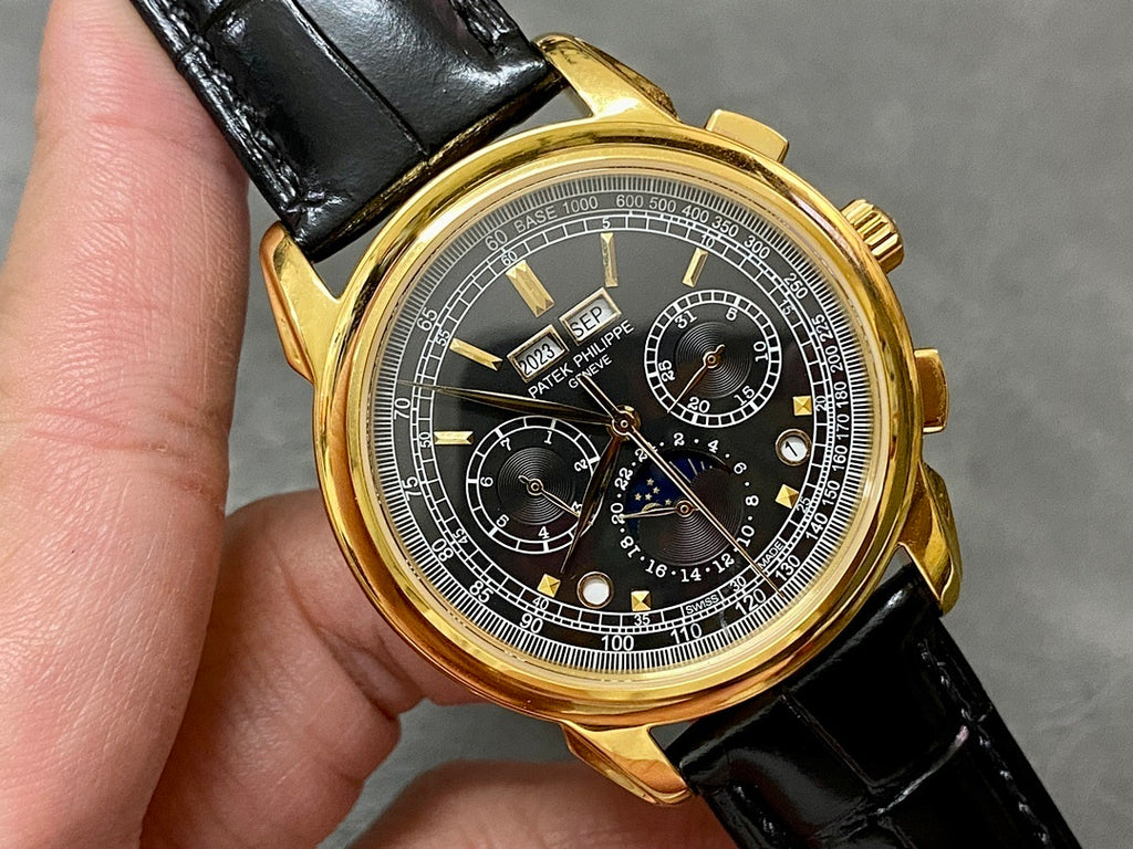 Close-up of gold watch face with black chronograph dial, subdials, and date area.