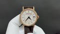 Gold wristwatch with white dial and brown leather strap, round case, baton markers