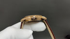 Gold wristwatch side view with crown and pushers, brown leather strap