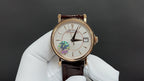 Gold-tone wristwatch on white glove with white dial and brown leather strap, left subdial