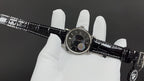Patek Philippe wristwatch on white glove with black dial and crocodile-style strap