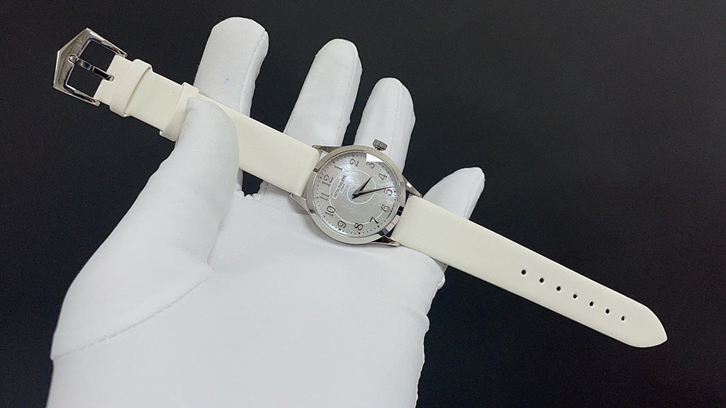 Wristwatch on light leather strap with buckle and perforations, held in white gloves