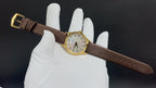 Brown leather strap watch on glove, gold buckle and dial visible