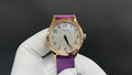 Gold wristwatch with purple leather strap, white dial and date window