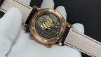 Luxury wristwatch close-up: black dial, black leather strap, gold case.