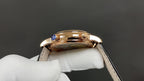 Luxury wristwatch crown side with blue gemstone, gold-tone case, black leather strap.
