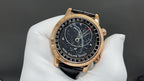 Luxury wristwatch front view with black dial, gold-tone case, black leather strap.