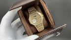 Gold-tone wristwatch in a brown leather display box with crown and dial visible