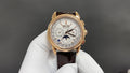 Gold-tone luxury wristwatch with white dial and brown leather strap, front view