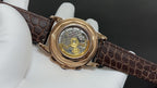 Gold-tone watch with transparent caseback, visible mechanical movement and brown leather strap
