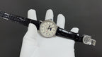 Wristwatch on black leather strap with clasp and small round dial at center