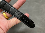 Black leather watch strap with stitching and glossy texture, held in a hand