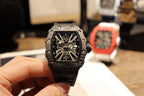 Richard Mille watch held up, front view of black square skeleton dial on strap