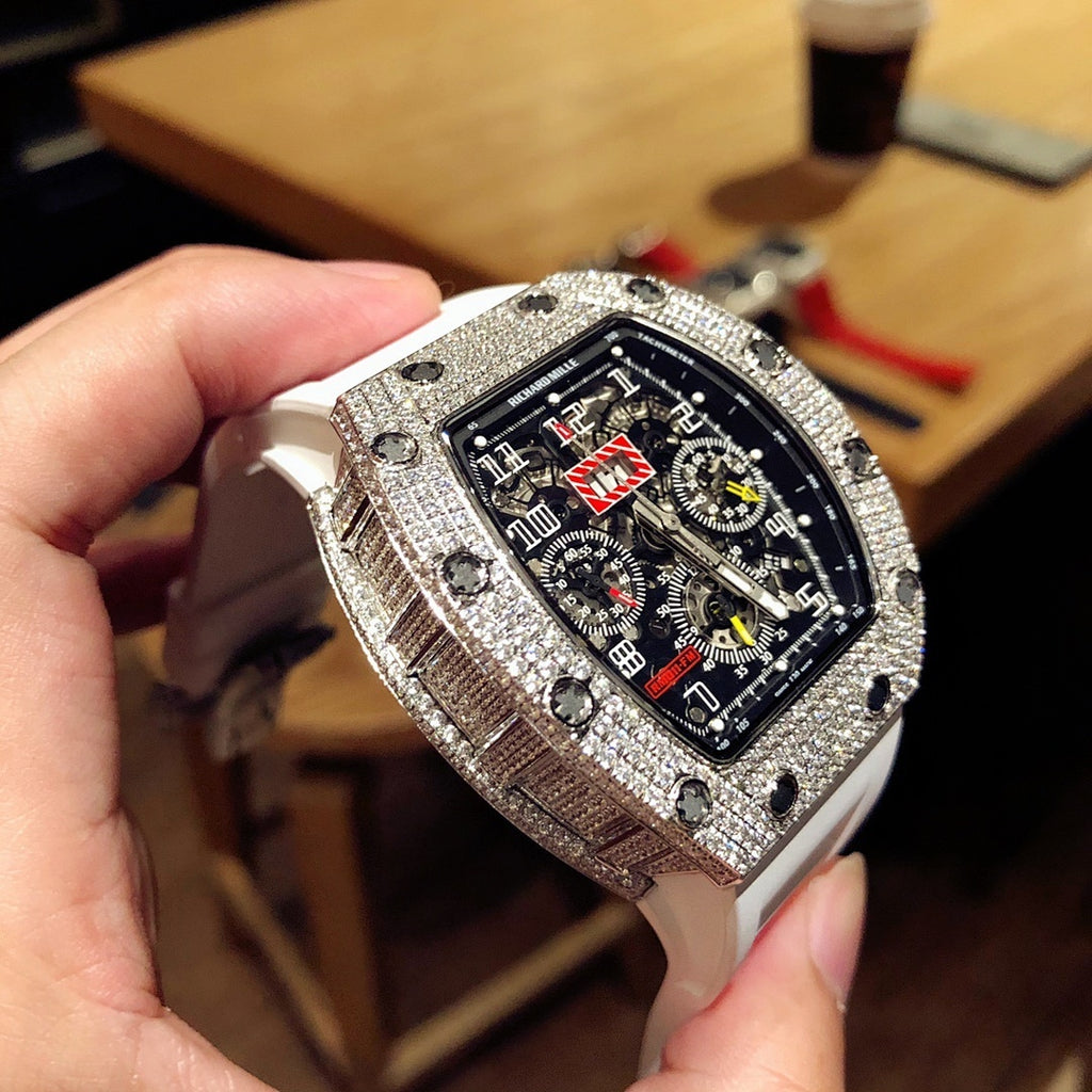 Square luxury watch with dark dial, jeweled bezel, and white rubber strap on hand