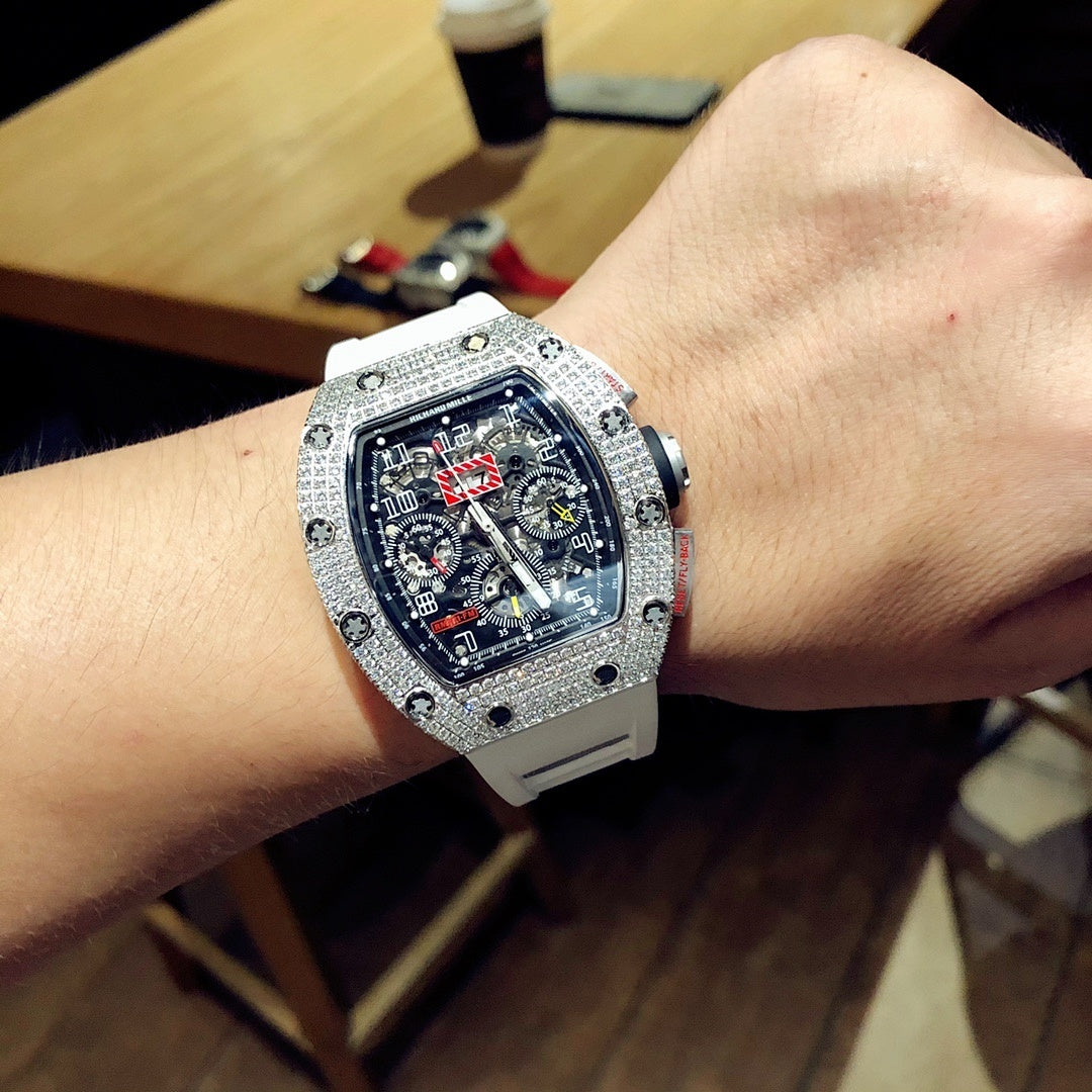 Square luxury watch on wrist with dark blue dial, jeweled bezel, and white rubber strap