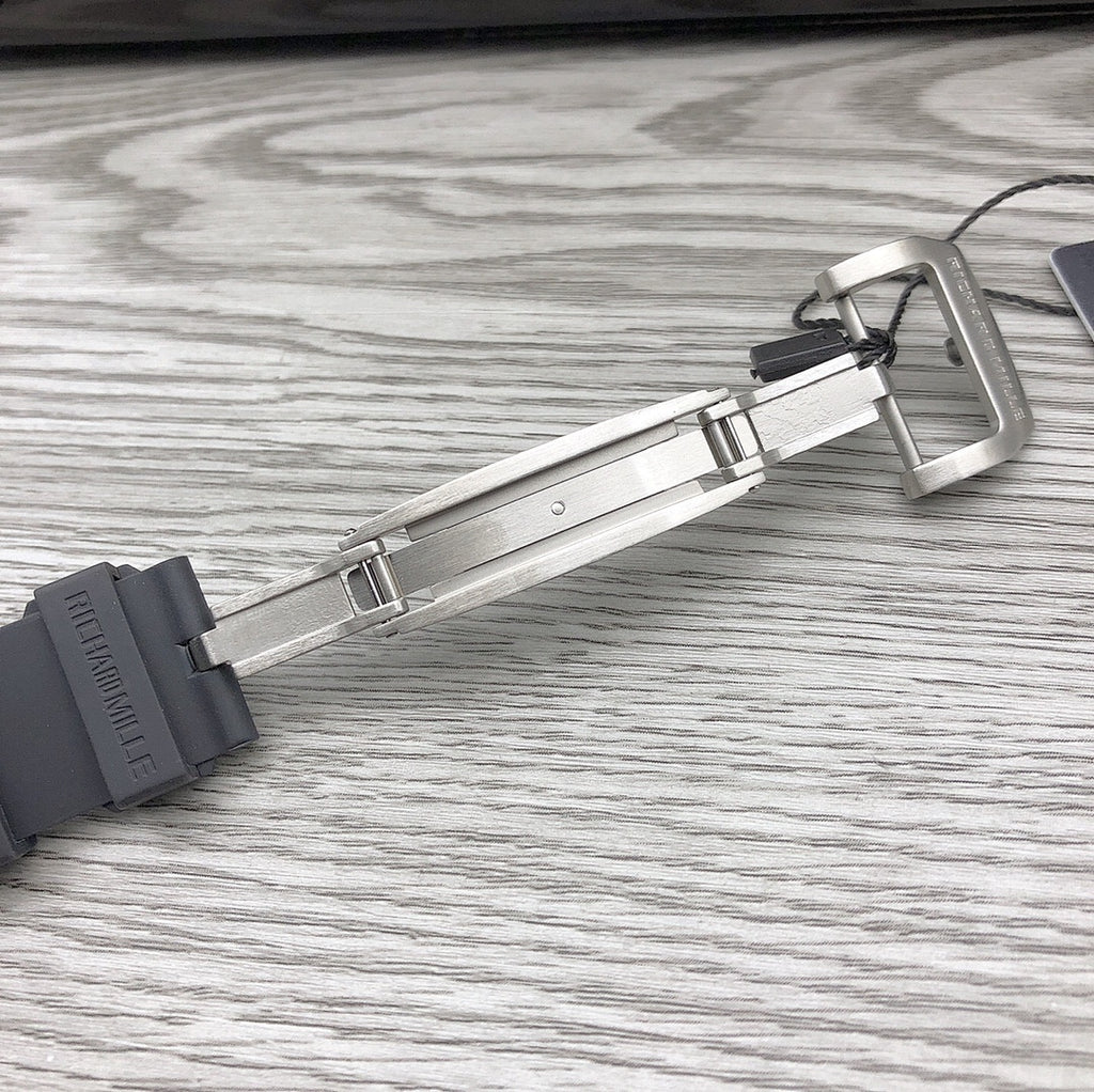 Black rubber watch strap with metal deployant clasp hardware laid on surface