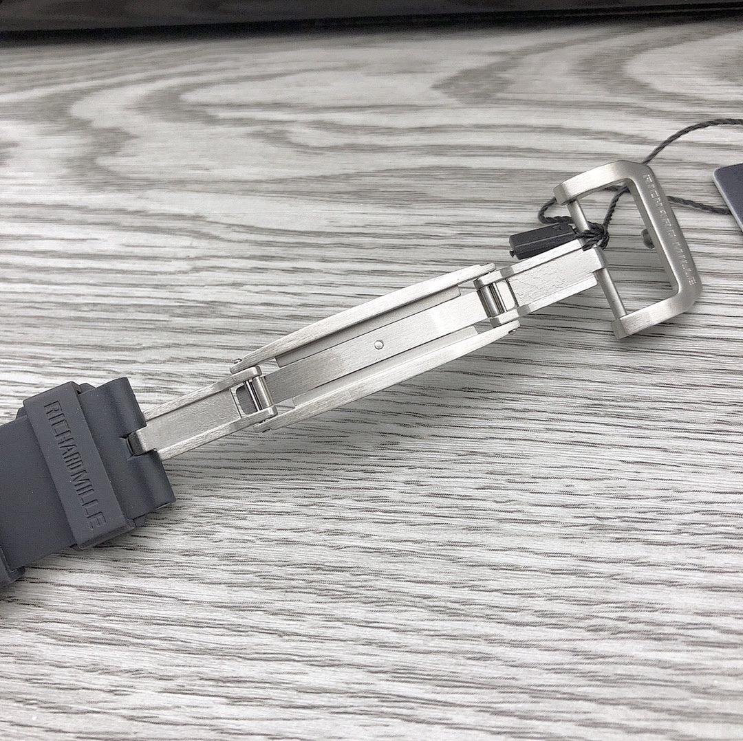 Black rubber watch strap with metal deployant clasp hardware laid on surface