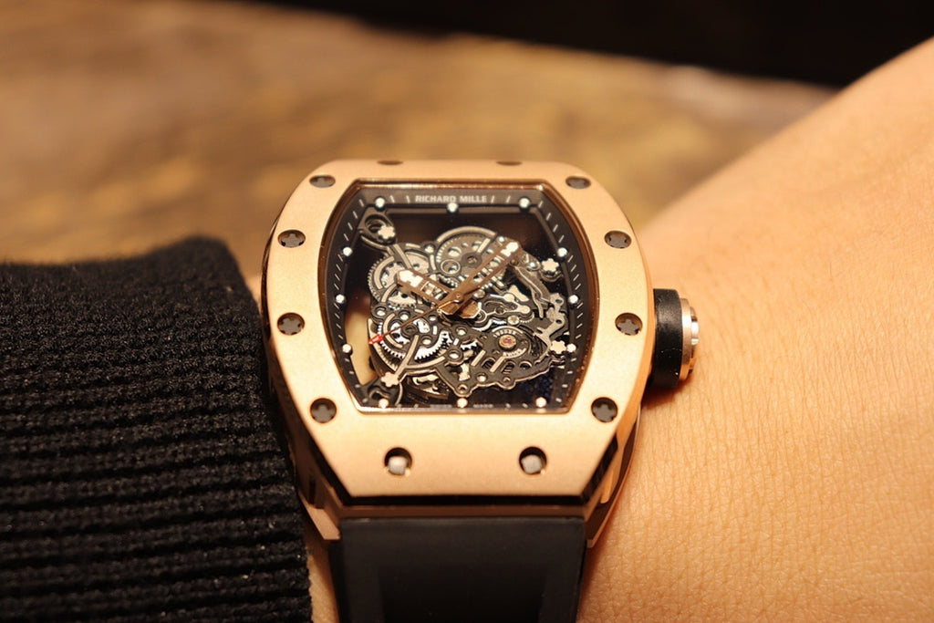 Gold-toned case watch with black rubber strap, straight-on view of skeleton movement