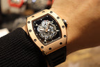 Gold-toned case watch with black rubber strap, close view of skeleton dial on wrist