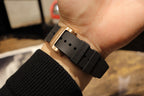 Gold-toned case watch with black rubber strap, clasp side view held in hand
