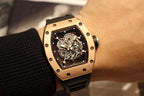 Gold-toned case watch with black rubber strap, skeleton dial shown on wrist
