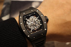 Black skeleton wristwatch on wrist, square case with screw details