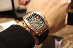 Rose gold-tone skeleton wristwatch close-up on wrist, black rubber strap