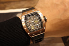 Rose gold-tone skeleton wristwatch with black rubber strap, angled front view
