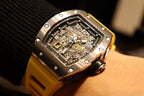 Richard Mille wristwatch close-up: yellow strap and black skeleton dial with metal bezel.