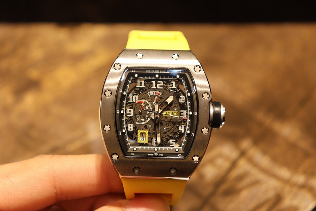 Richard Mille wristwatch held up: yellow strap and black dial with visible subdials.