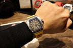 Richard Mille wristwatch on wrist: yellow rubber strap with black dial and metal bezel.