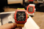 Red skeleton tourbillon watch held in hand with black dial and yellow strap