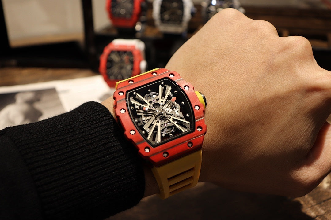Red skeleton tourbillon watch with black dial on wrist, yellow rubber strap