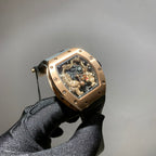 Richard Mille watch with gold-toned case, black strap, and skeleton dial with rotating gears