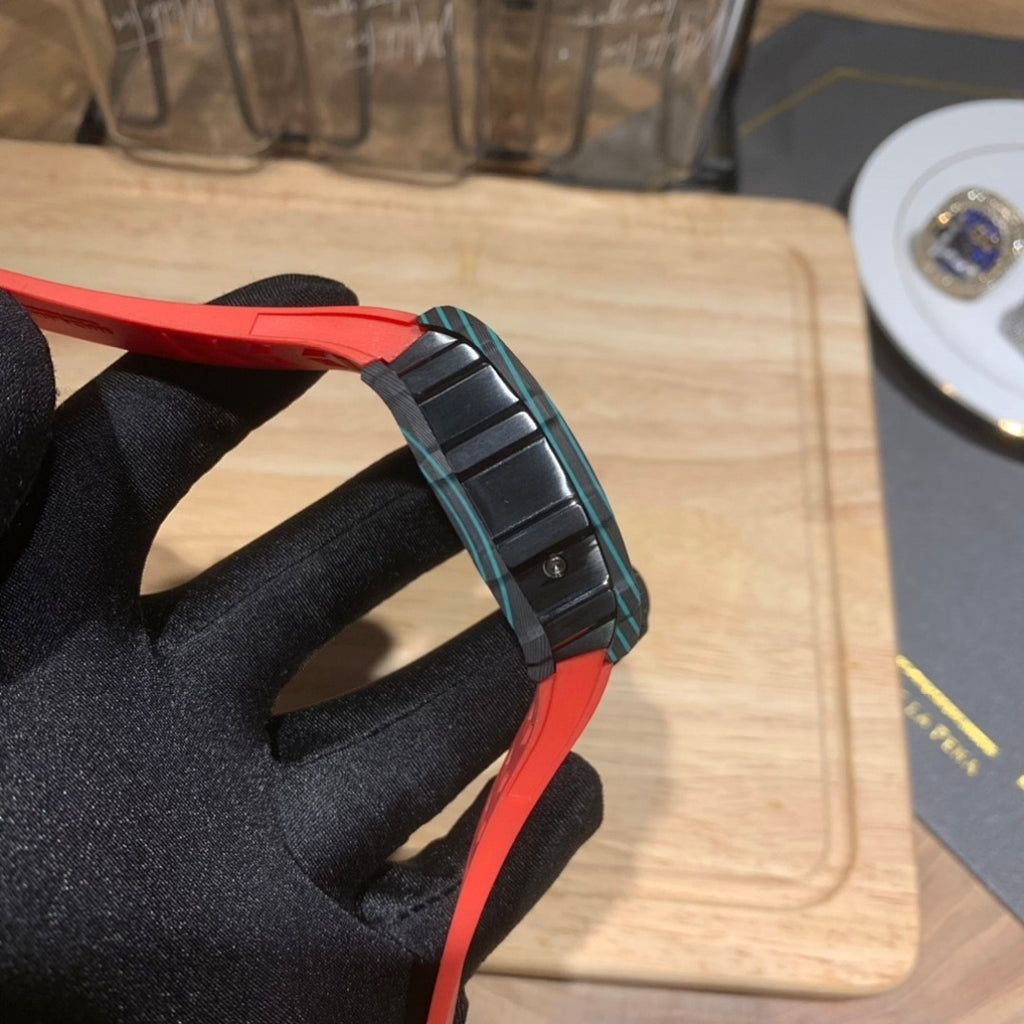 Richard Mille watch side view with black and teal case accents and red strap.