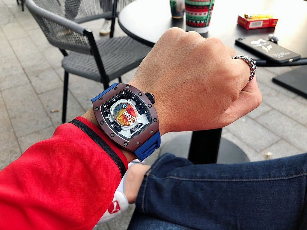 Richard Mille watch with blue strap on wrist, square dark case, skeleton dial