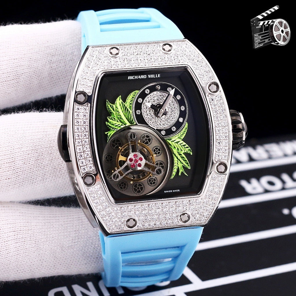 Silver-toned watch with light blue silicone strap; dark dial with green leaf art and skeleton movement.