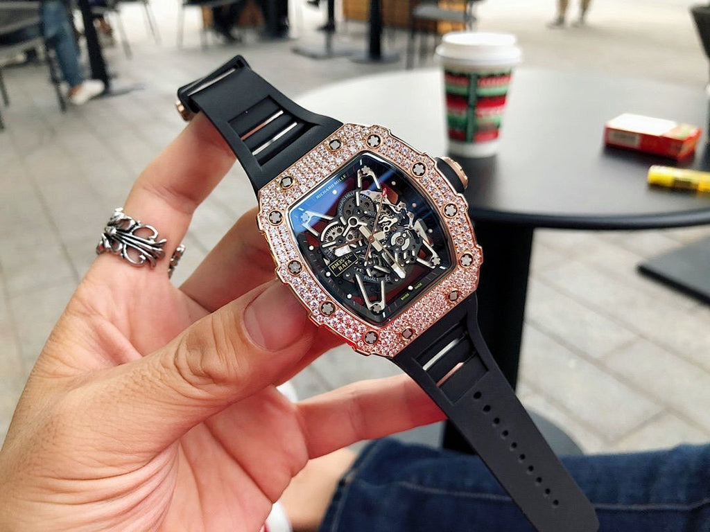 Richard Mille watch with jeweled bezel, dark skeleton dial, black strap on hand.