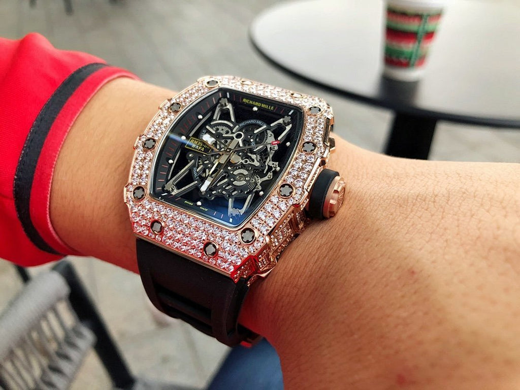 Richard Mille watch with jeweled bezel, dark skeleton dial, black strap with red accents.