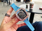 Men’s jeweled skeleton watch with light blue silicone strap held in hand, black dial
