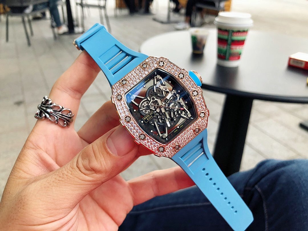 Men’s jeweled skeleton watch with light blue silicone strap held in hand, black dial
