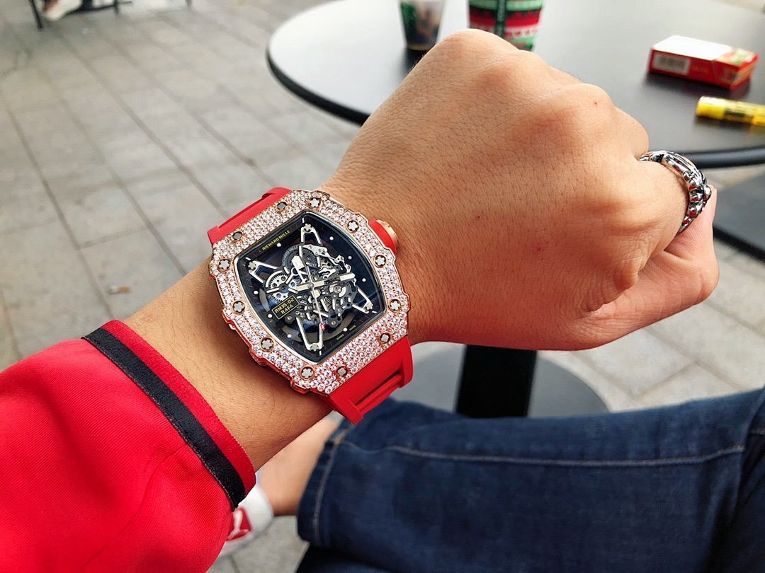 Men’s jeweled skeleton watch with red silicone strap on wrist, black dial