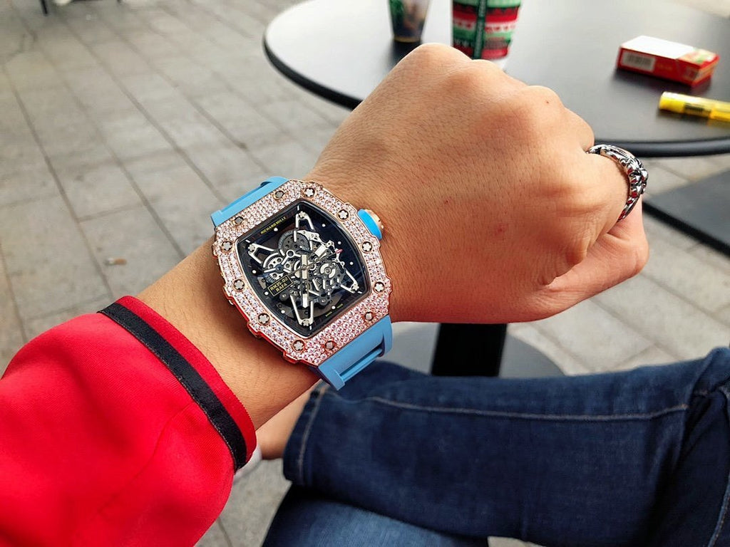 Men’s jeweled skeleton watch with light blue silicone strap on wrist, black dial