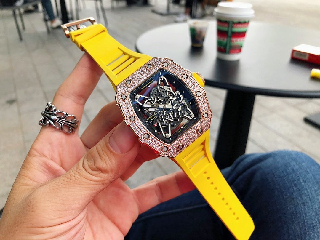 Men’s jeweled skeleton watch with yellow and red silicone straps held in hand, black dial