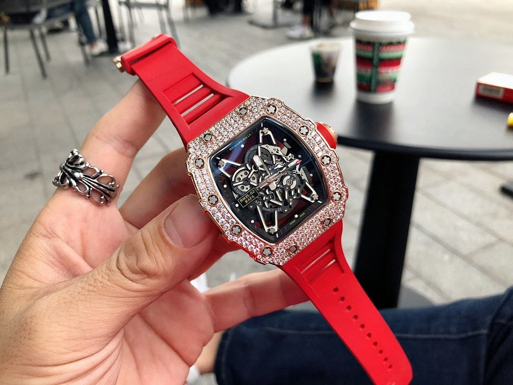 Men’s jeweled skeleton watch with red silicone strap held in hand, black dial
