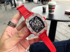 Men’s jeweled skeleton watch with red silicone strap held in hand, black dial