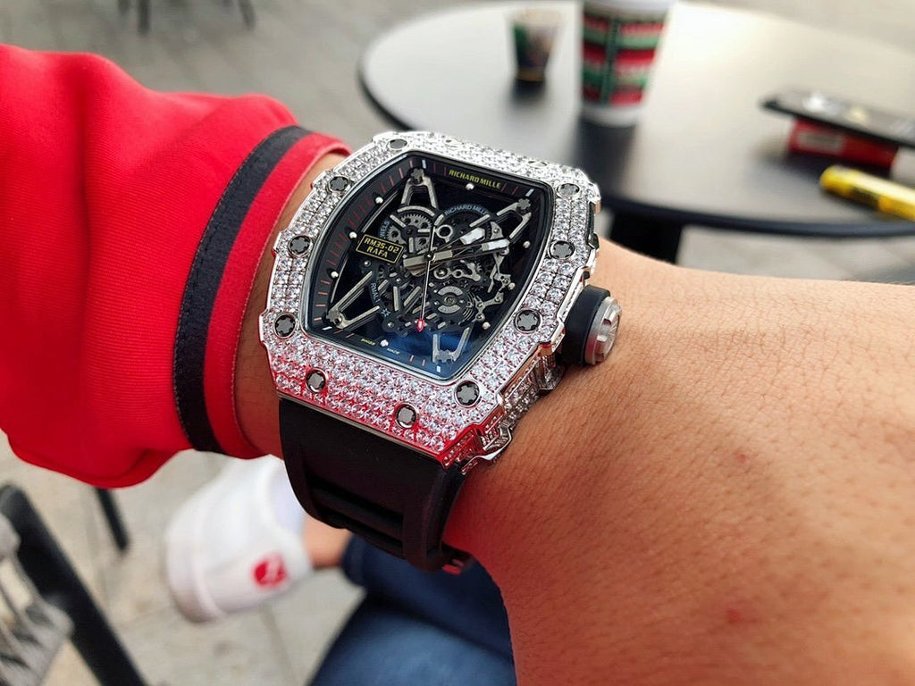 Richard Mille watch on wrist with black strap and jeweled silver case
