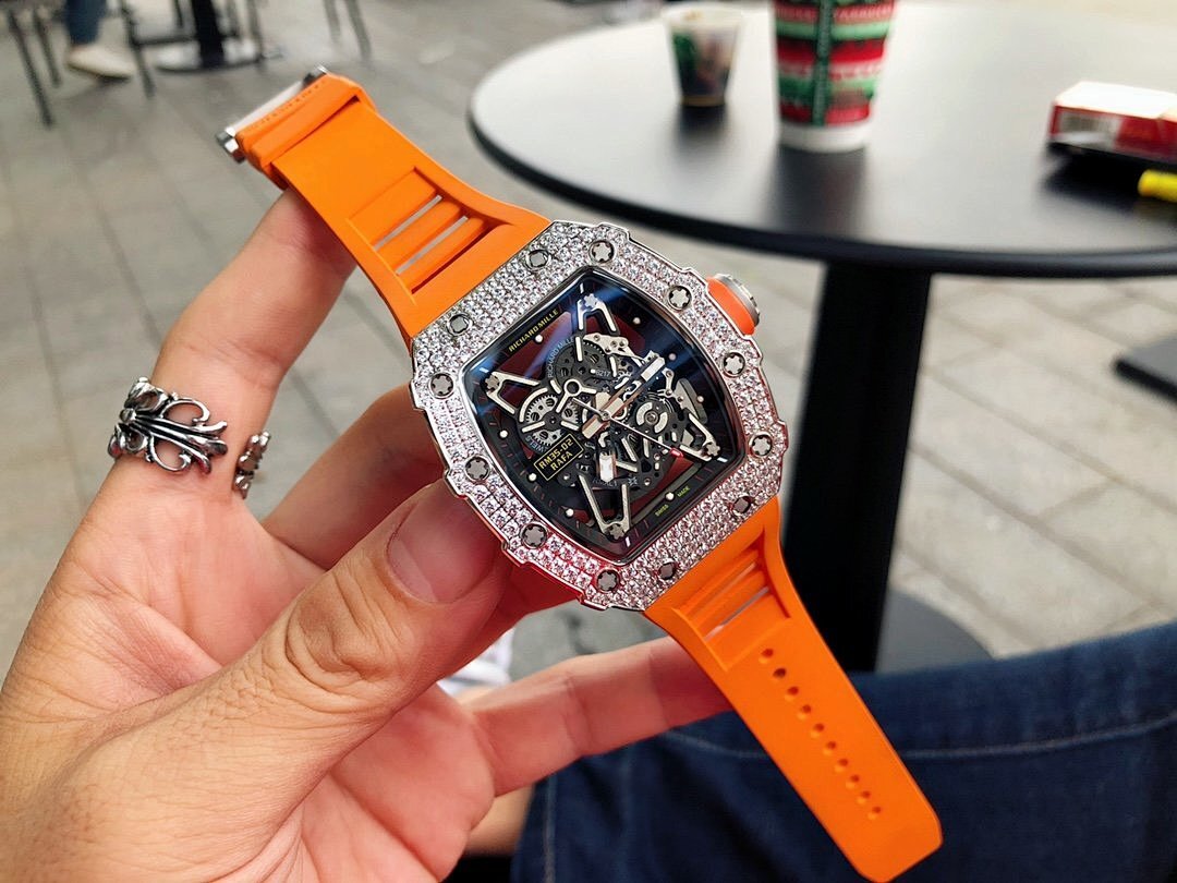 Richard Mille watch with silver gem-set bezel, orange rubber strap, visible mechanical dial.