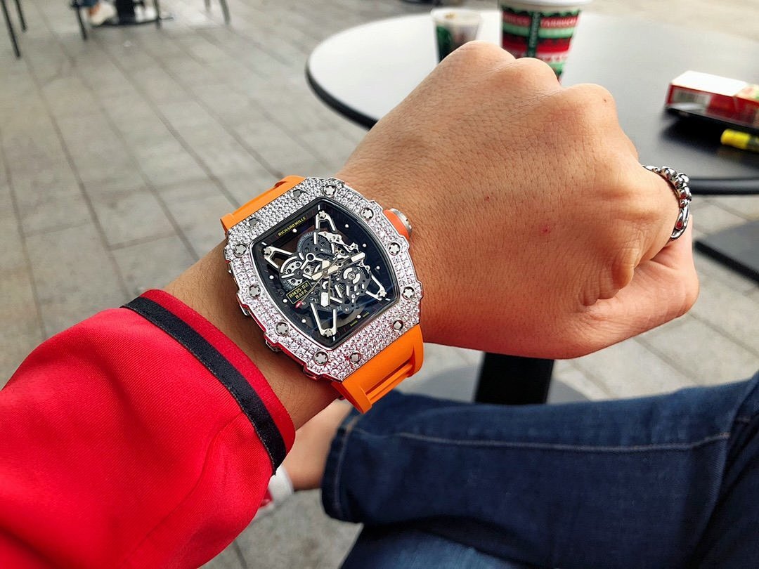 Richard Mille watch on wrist with silver gem-set bezel and orange rubber strap.